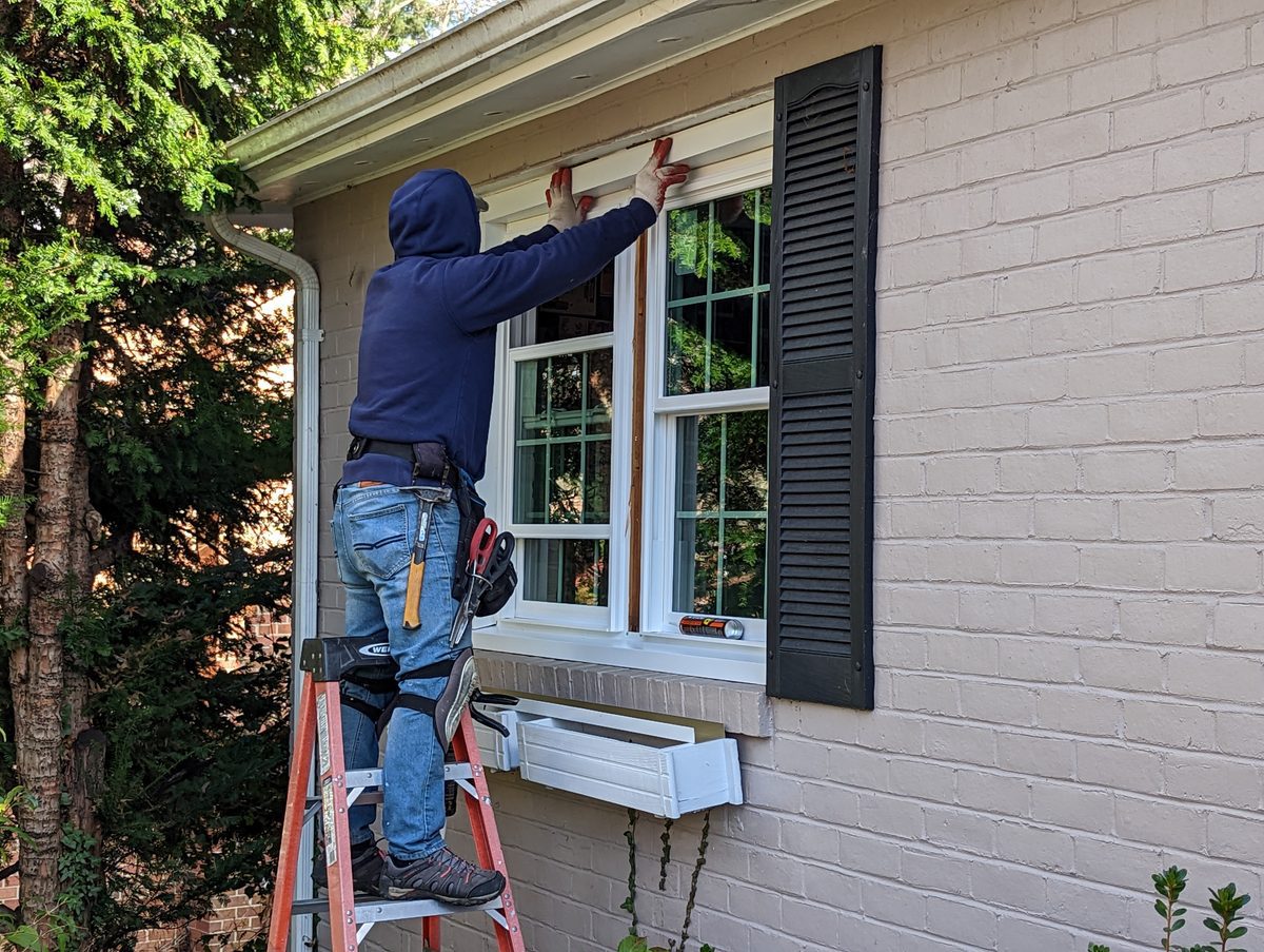 Hallmark crew member installing a Vytex double-hung window with colonial grids from a ladder