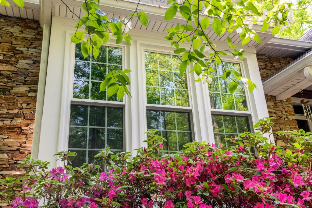 Three Vytex Potomac-HP double-hung windows with colonial grids on a stone home with azaleas